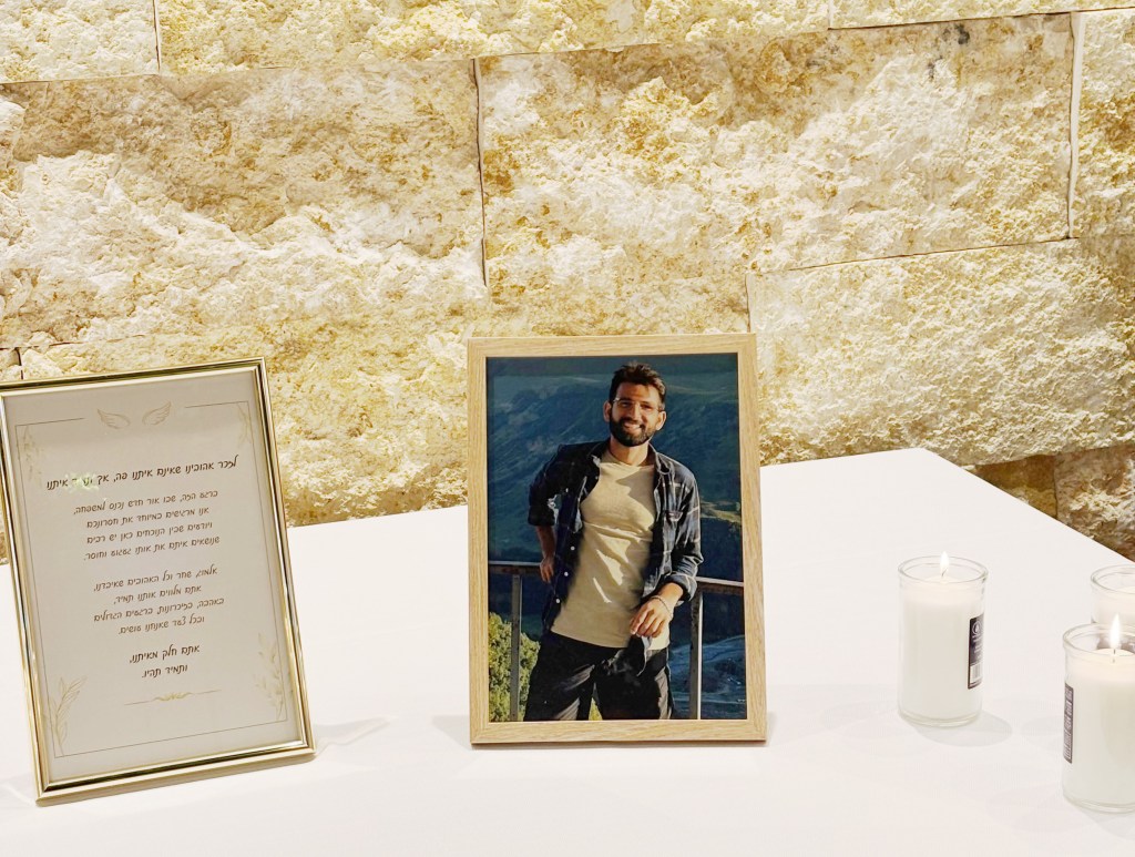 Almog Sarusi, killed at age 27, in a framed photo on a table with memorial candles and a framed message.