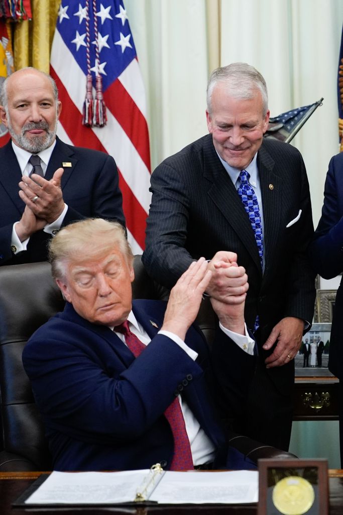 President Donald J. Trump shakes hands with U.S. Senator Dan Sullivan in the Oval Office, as Secretary of Commerce Howard Lutnick looks on.