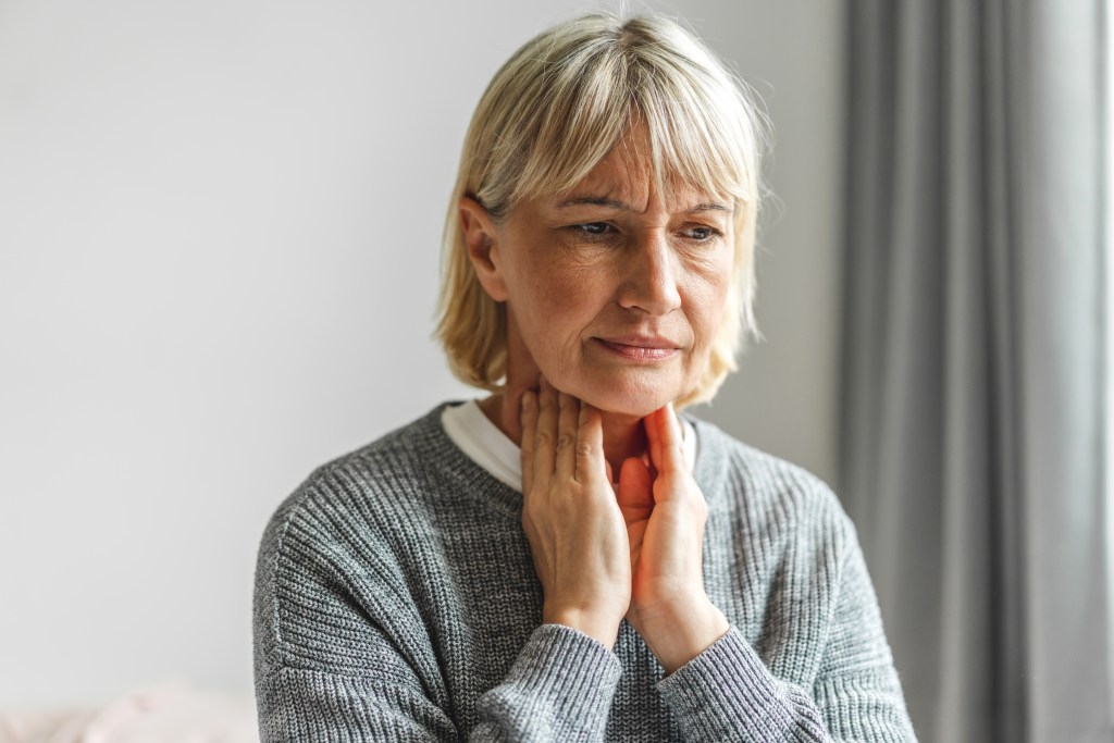 An elderly woman with a sore throat touching her neck.