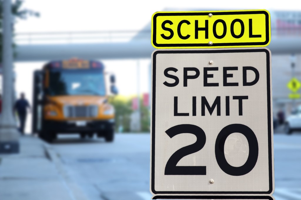 A school zone warning sign and speed limit 20 sign with a school bus in the background.