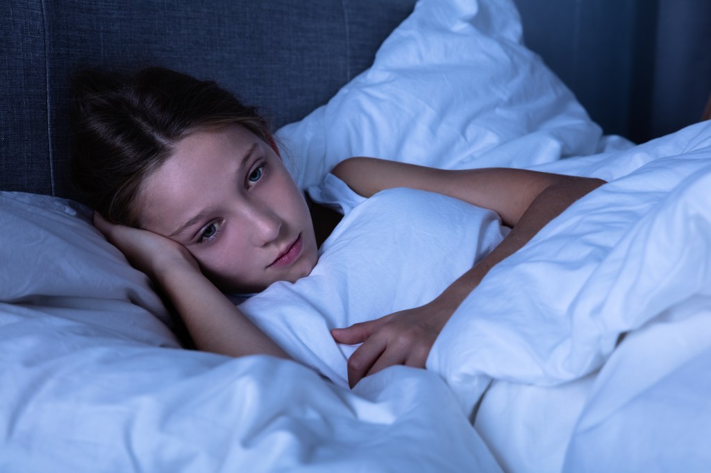 A young girl suffering from insomnia lies awake in bed at night.