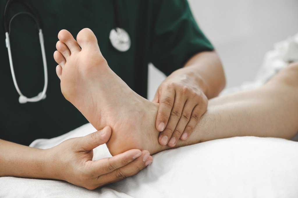 A physiotherapist examining and treating a patient's injured ankle in a clinic.