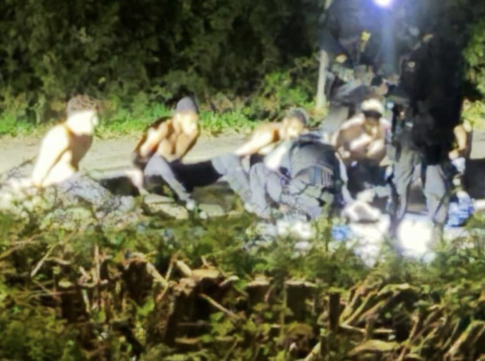 Several men are arrested at gunpoint outside at night by armed officers.